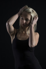 Fototapeta premium Beautiful blond woman in black top in dark with selective lighting and hands in hair