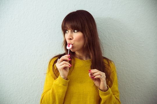 Frau mit gelbem Pulli lutscht an Herzlolli