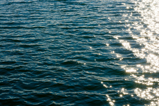 Sea ripples. Bright background. Dark green water. Shallow waves and sun glare on the water. Abstract.