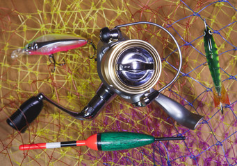 The coil, float and baits on a fishing net background.