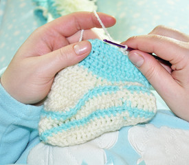 knitted baby socks of white and blue acrylic yarn. handmade clothes. on a blue background is a ball of yarn and related products. lesson crochet, air loop, column, openwork pattern.