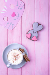 Coffee cappuccino with cinnamon and gingerbread rabbit with heart on a pink wooden background. Happy Valentine's Day!
