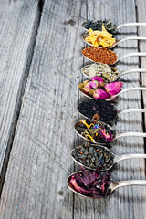 Various kinds of tea in spoons on wooden background. Dry Tea assortment.