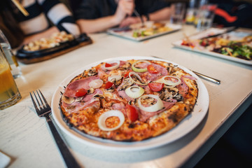 Delicious pizza with tomato and onion on the white plate at the restaurant while friends having lunch.