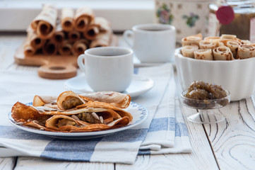 Thin pancakes for breakfast. Maslenitsa. On the table, a dish with pancakes, coffee and jam from feijoa