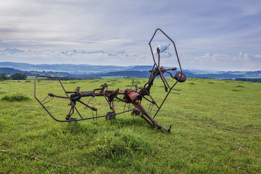 Rusty hay turner on a meadow in Broumov Highlands in Czech Republic