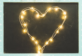 Top view of a blackboard or chalkboard with a led light heart shaped garland, vintage toned. Love,...