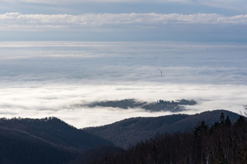 Fototapeta na wymiar Landscape view from Sljeme or Medvednica mountain down on clouds covering the city of Zagreb in Croatia with a visible smoking heat plant chimney above the clouds during sunrise