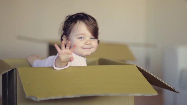 Laughing child girl sitting in cardboard boxe in her new home.