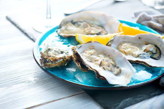 Fresh oysters close-up on blue plate, served table with oysters, lemon and champagne in restaurant. Gourmet food