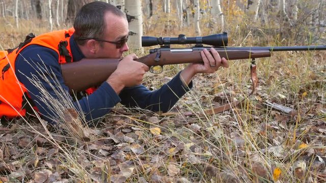 Hunter looks through his scope on rifle in the aspen trees