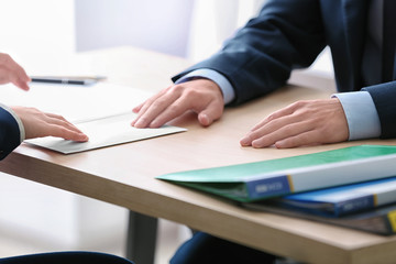 Man giving money in envelope to businessman at table. Corruption concept