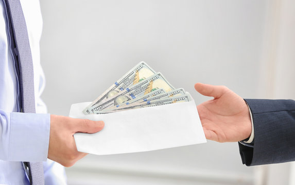 Businessman taking money in envelope from man on light background