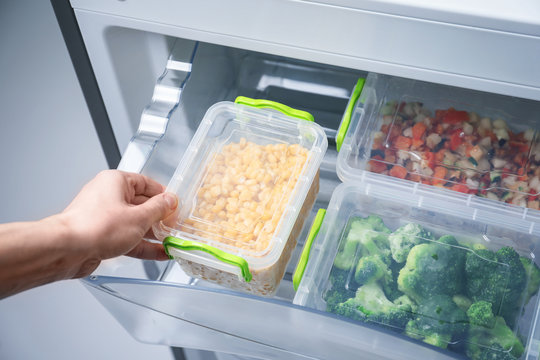 Woman taking container with frozen corn from refrigerator