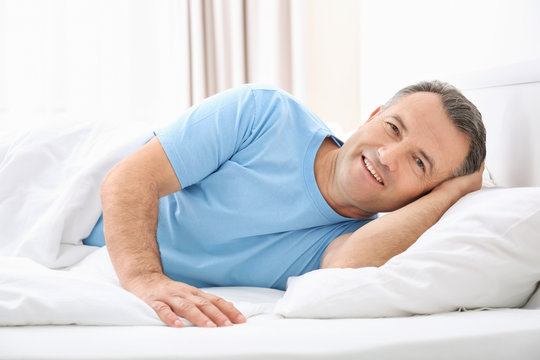 Mature man lying on white pillow indoors