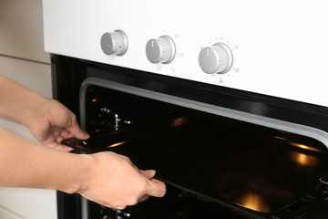 Young woman taking baking pan out of modern electrical oven in kitchen