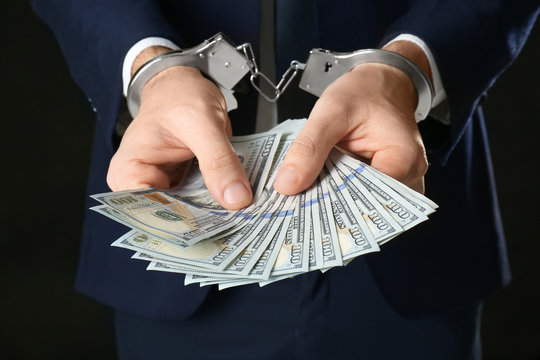 Businessman in handcuffs holding bribe, closeup
