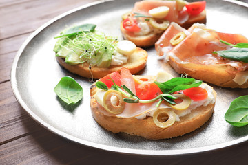 Tasty bruschettas with prosciutto and olives on plate