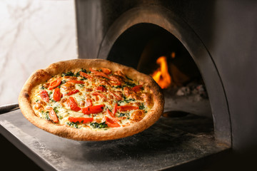 Taking traditional pizza out of oven in restaurant kitchen