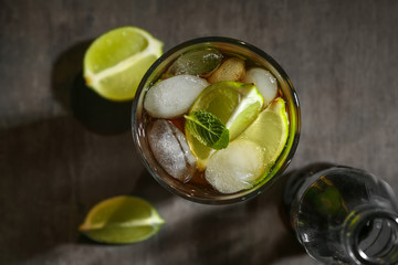 Glass with Cuba Libre cocktail and bottle of cola on table