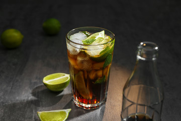 Glass with Cuba Libre cocktail and bottle of cola on table