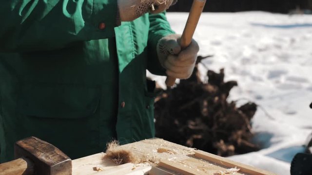 Close up hand in worker gloves hammering wood kernel to hole in wooden block outside in winter, snow on background