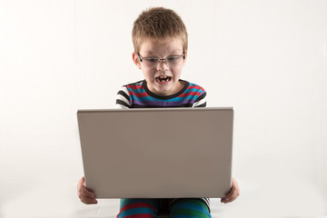 A Caucasian boy with glasses tries to work with a computer and the Internet. The guy gets vivid emotions.