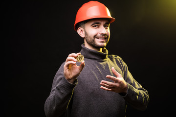 Handsome man miner in protective hemlet present bitcoin isolated on black background