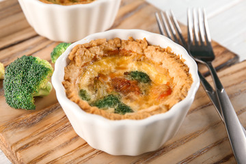 Ramekin with tasty broccoli quiche on wooden board, closeup