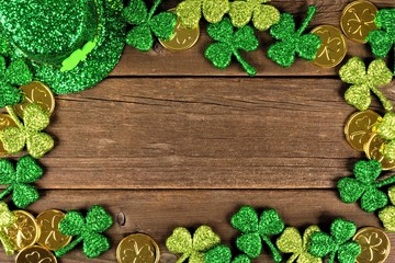 St Patricks Day frame of shamrocks, gold coins and leprechaun hat over rustic wood