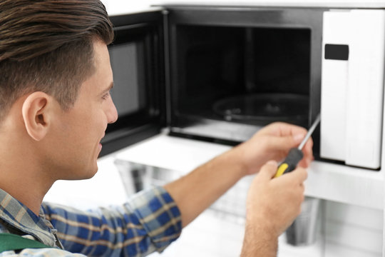 Young man repairing microwave oven, closeup