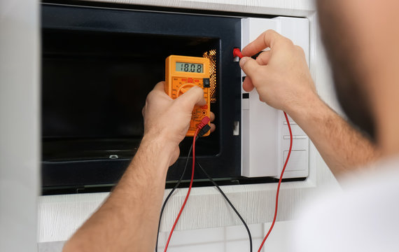 Young man repairing with multimeter microwave oven, closeup