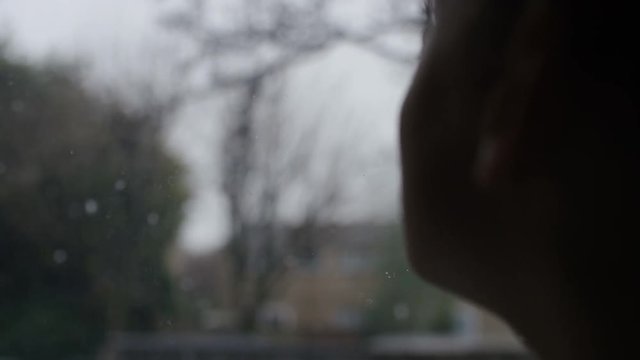 Young child sitting by a window looks at the snow outside, in slow motion
