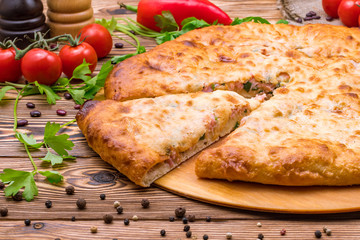 Piece of Ossetian cheese and ham pie on a wooden background 