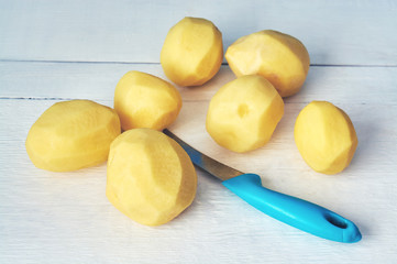 Peeled potatoes and a knife on white wooden background