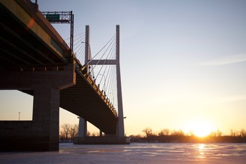 Sun rising besides a bridge over a frozen river