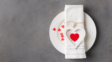 Valentines day meal background with white wood vintage heart  and red candy hearts, white plate and napkin. Romantic holiday table setting. Concrete background with blank. Restaurant concept. Flat lay