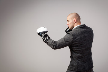 Young bald man, confident business man in white shirt, gray suit and boxing gloves box on white isolated background, side view