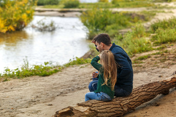 Father and daughter are sitting on a fallen tree