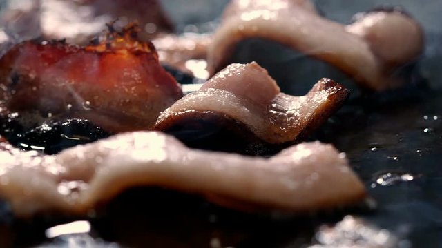 Bacon Frying - Slow motion macro panning video of pork bacon frying on black griddle. 