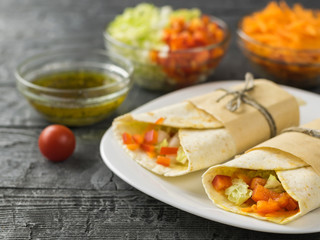 Two vegetable roll tortilla from wheat flour in white bowl on a wooden table with herbs.