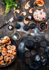 Fototapeta na wymiar Preparation of Italian black ravioli with seafood shrimps and crabs on black plate, gray stone slate background. Top view