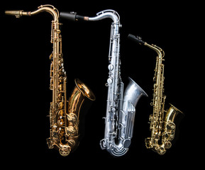 Full view of three saxophones standing isolated in black