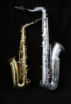 Full view of two saxophones standing isolated in black