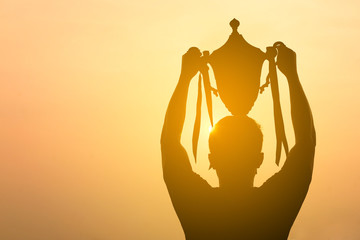 silhouette of a man holding up trophy on sunset sky