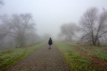 Woman walking on a dirt road in the fog into the unknown