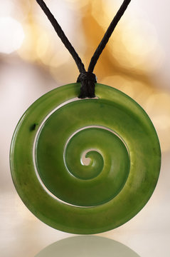 Gr&uuml;ne Jade Spirale als Symbol Schmuck Schmuckstein Anh&auml;nger Koru aus Neuseeland mit Bokeh Hintergrund.