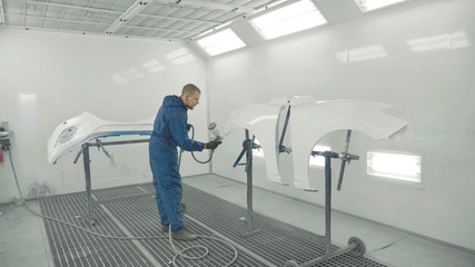 Auto painter spraying white paint on car spare fender in special booth