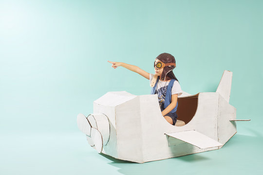 Little cute girl playing with a cardboard airplane. White retro style cardboard airplane on mint green background . Childhood dream imagination concept .