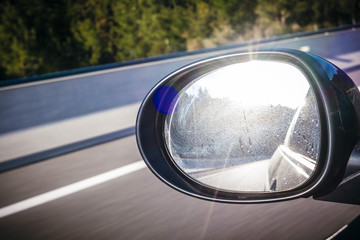 Sun shining on a left black mirror car on a highway